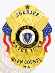 A custom metal badge in gold featuring the title "SHERIFF" prominently at the top, with a central eagle emblem above the words "COMM. OF MASSACHUSETTS." The badge displays "WATER TOWN" in bold letters, with "GLEN COUNTY MA" below. It is adorned with decorative blue and red elements, enhancing its vibrant design. The polished gold finish gives the badge an official appearance, signifying its importance in law enforcement and its role in the community.